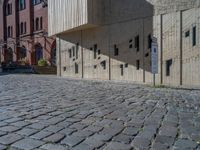 cobblestone driveway surrounded by modern buildings on sunny day with sun reflecting onto the windows