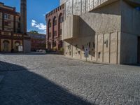 cobblestone driveway surrounded by modern buildings on sunny day with sun reflecting onto the windows