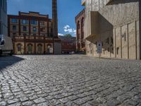 cobblestone driveway surrounded by modern buildings on sunny day with sun reflecting onto the windows