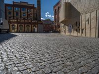 cobblestone driveway surrounded by modern buildings on sunny day with sun reflecting onto the windows