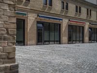 the sidewalk is paved with stones and has a bench in front of it, with no people inside