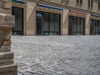 the sidewalk is paved with stones and has a bench in front of it, with no people inside