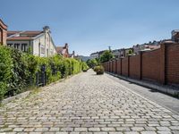 a cobblestone driveway in the middle of a neighborhood with a gated sidewalk and two brick houses behind it