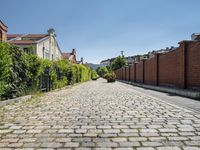 a cobblestone driveway in the middle of a neighborhood with a gated sidewalk and two brick houses behind it