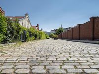 a cobblestone driveway in the middle of a neighborhood with a gated sidewalk and two brick houses behind it