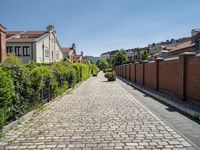 a cobblestone driveway in the middle of a neighborhood with a gated sidewalk and two brick houses behind it