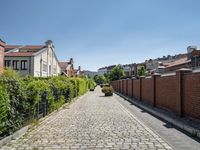 a cobblestone driveway in the middle of a neighborhood with a gated sidewalk and two brick houses behind it