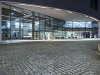 the empty bench has lights on as it sits on cobblestone pavement in front of a building