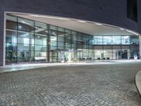 the empty bench has lights on as it sits on cobblestone pavement in front of a building