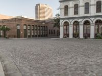 a cobblestone paved plaza and buildings in the middle of downtown with a city skyline