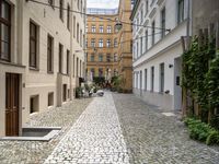 a cobblestone road with a bench in between the buildings and benches on each side