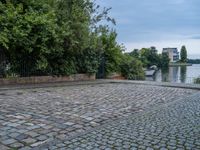 a brick road that has a boat in the distance and some bushes on the other side