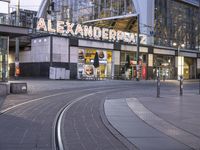 the building that says alexandria plaza in english is next to a train track on a city street