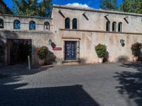 this is a cobblestone road that has a house with arched windows and potted planters