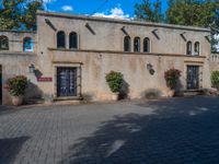 this is a cobblestone road that has a house with arched windows and potted planters