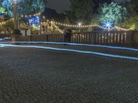 a person is standing on an empty brick walkway by the tv tower and trees with lights