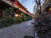 a brick sidewalk with stone pathway between buildings and trees in a chinese city area with red lanterns hanging on the buildings