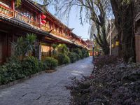 a brick sidewalk with stone pathway between buildings and trees in a chinese city area with red lanterns hanging on the buildings