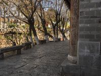 an empty bench sits on a cobblestone street next to some trees and a hill