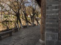 an empty bench sits on a cobblestone street next to some trees and a hill