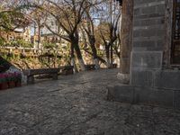 an empty bench sits on a cobblestone street next to some trees and a hill