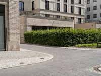 a sidewalk with cobblestone walkway next to a building and trees and bushes and a bench