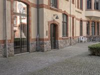 people walk by two buildings next to them with benches and trees in the courtyard nearby