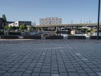 a brick paved walkway with a bridge and a river in the background next to a cement block wall