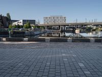 a brick paved walkway with a bridge and a river in the background next to a cement block wall