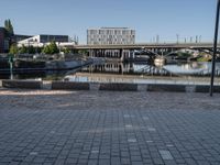 a brick paved walkway with a bridge and a river in the background next to a cement block wall