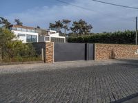 a driveway with a brick wall and an asphalt block on the side of it with a grey gate in front of it