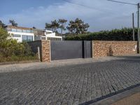 a driveway with a brick wall and an asphalt block on the side of it with a grey gate in front of it