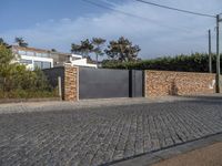 a driveway with a brick wall and an asphalt block on the side of it with a grey gate in front of it