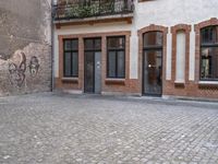 this is an image of two people walking on a cobble stone street by some brick buildings