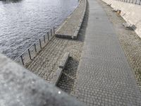 a path that is by the water and has benches lined along it with a bench to either side