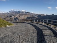 an image of a cobblestone roadway near a mountain range in italy with a long curved bridge