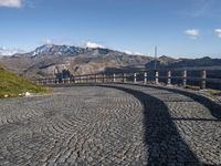 an image of a cobblestone roadway near a mountain range in italy with a long curved bridge