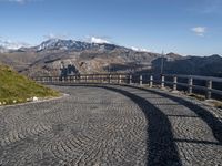 an image of a cobblestone roadway near a mountain range in italy with a long curved bridge