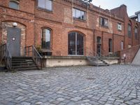 the brick sidewalk has some stairs in it near a building with stairs going up to the top