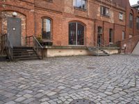 the brick sidewalk has some stairs in it near a building with stairs going up to the top