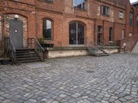 the brick sidewalk has some stairs in it near a building with stairs going up to the top