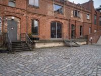 the brick sidewalk has some stairs in it near a building with stairs going up to the top