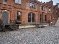 the brick sidewalk has some stairs in it near a building with stairs going up to the top