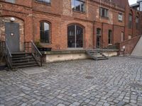 the brick sidewalk has some stairs in it near a building with stairs going up to the top