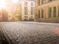 someone riding a skateboard on a cobblestone sidewalk near buildings with a bike in it