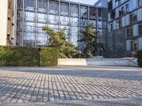 the sidewalk is cobbled in with bushes and bushes in front of a building with many windows