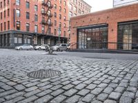 a cobble stone sidewalk with some parked cars and buildings in the background by a street hydrant