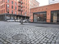 a cobble stone sidewalk with some parked cars and buildings in the background by a street hydrant