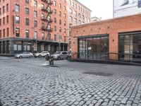 a cobble stone sidewalk with some parked cars and buildings in the background by a street hydrant