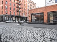 a cobble stone sidewalk with some parked cars and buildings in the background by a street hydrant